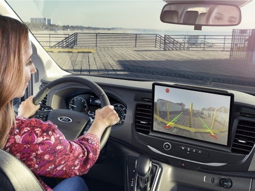 2024 Ford Transit view of woman driving using rear camera to back into a parking spot