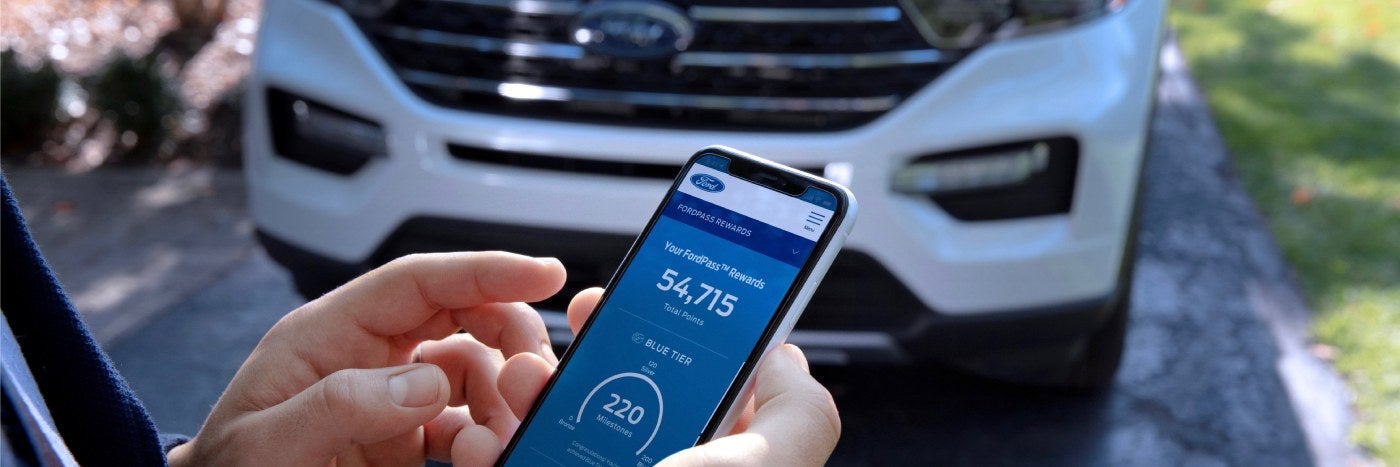 Close up view of a phone with the FordPass Rewards app open and a Ford vehicle in the background